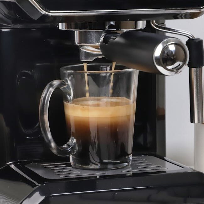 A close-up view of espresso being poured into a glass from a coffee machine, showcasing rich crema.